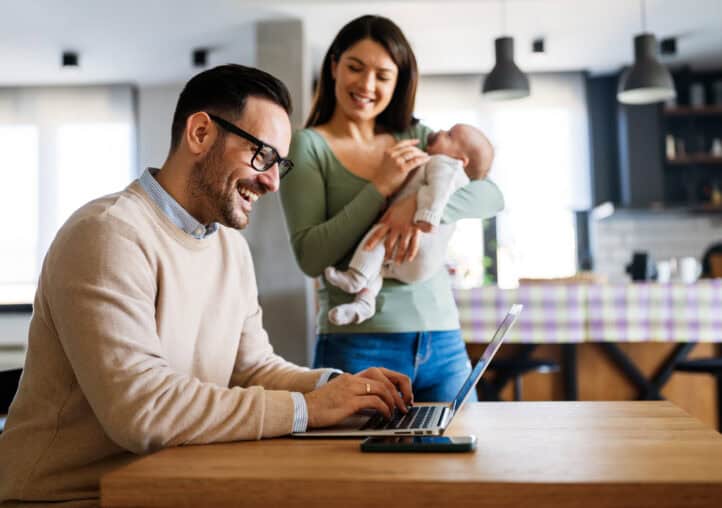 portrait of young couple with a baby at home, using laptop. father is trying to work from home.