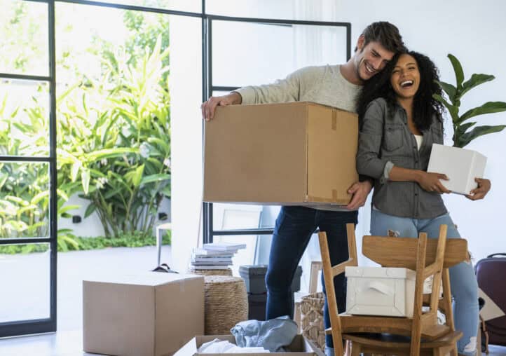 couple carrying cardboard box and pot plant in new house