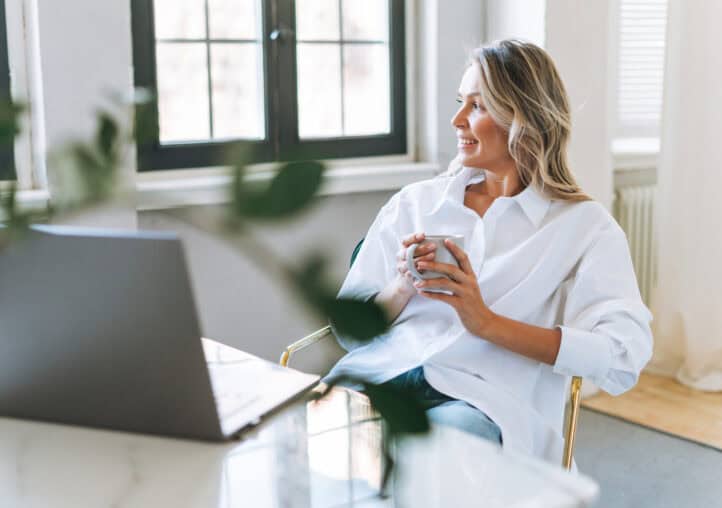 young smiling blonde woman with long hair in white shirt rest and drinking tea in the bright modern office
