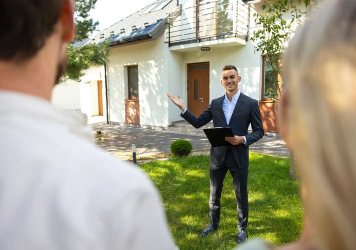 agent showing new home to clients in suburban garden setting. Auction